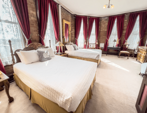 Bright, spacious bedroom with two beds, large windows, and elegant red curtains, featuring vintage decor and soft lighting.