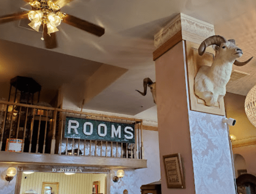 Interior of a rustic lodge featuring a "ROOMS" sign, a mounted ram's head, and vintage decor.