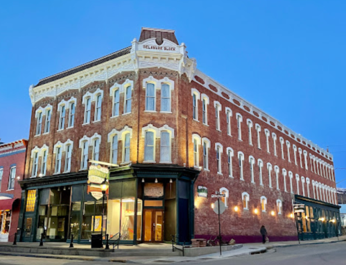 Historic brick building with ornate details, illuminated at dusk, located on a street corner.