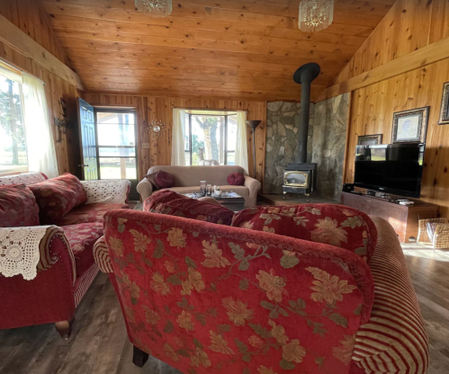 Cozy living room with wooden walls, a stone fireplace, and vintage furniture, featuring red floral upholstery.