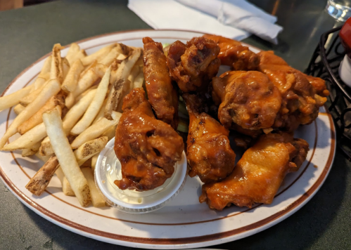 A plate of crispy chicken wings coated in sauce, served with a side of golden French fries and a small cup of dipping sauce.