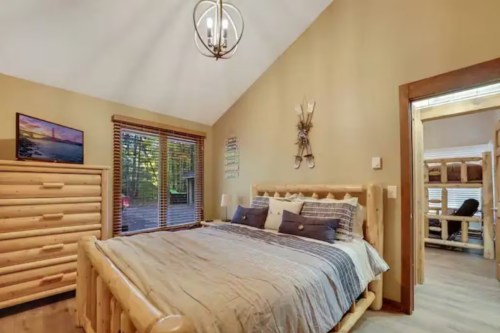 Cozy bedroom with a log bed, warm lighting, and large windows overlooking nature.