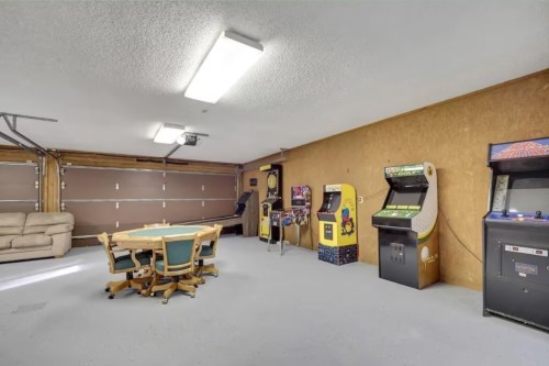 A spacious garage with arcade machines, a round table with chairs, and a couch against the wall.
