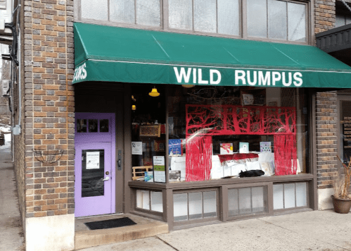 A storefront with a green awning reading "WILD RUMPUS," featuring colorful displays and a purple door.