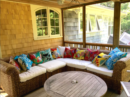 Cozy screened porch with a wicker sectional sofa adorned with colorful patterned pillows and a round wooden table.