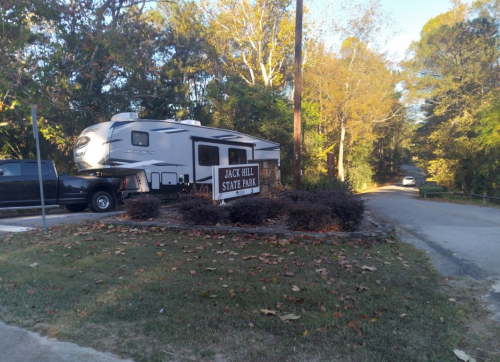 A camper parked near a sign for Jack Hill State Park, surrounded by trees and autumn foliage.