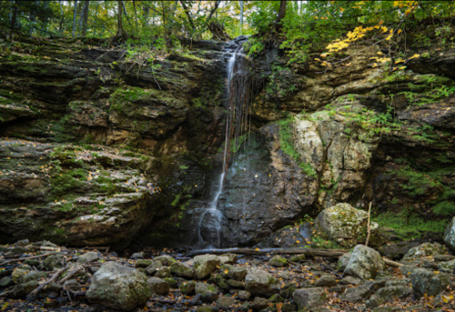 A serene waterfall cascading down a rocky cliff, surrounded by lush green foliage and moss-covered stones.