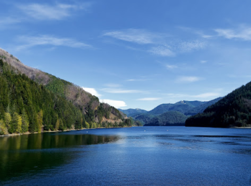A serene lake surrounded by lush green hills under a clear blue sky.