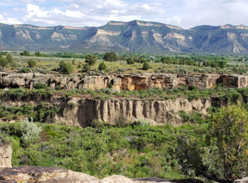 A scenic view of rugged cliffs and green vegetation with mountains in the background under a partly cloudy sky.