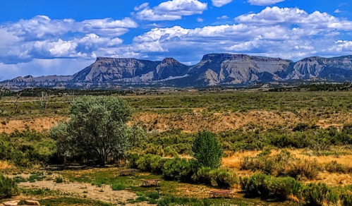 A scenic view of mountains under a blue sky with clouds, surrounded by sagebrush and grassy terrain.