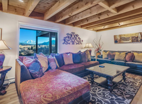 Cozy living room with a large sectional sofa, coffee table, and scenic mountain view through a window. Warm, inviting decor.