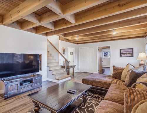 Cozy living room with wooden beams, a large sofa, TV, and staircase leading to an upper level.