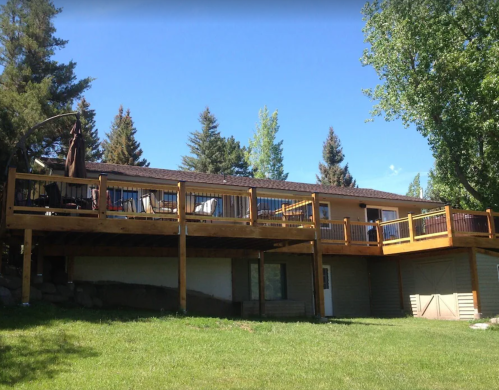 A wooden deck extends from a house surrounded by trees, with outdoor furniture visible on the deck.