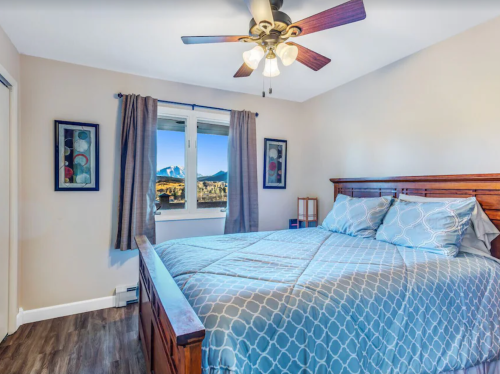 Cozy bedroom with a wooden bed, blue bedding, ceiling fan, and mountain view through a window.