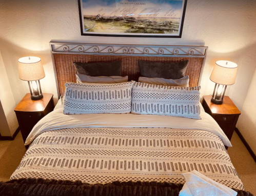 Cozy bedroom with a patterned bedspread, two lamps, and a decorative headboard. Warm and inviting atmosphere.