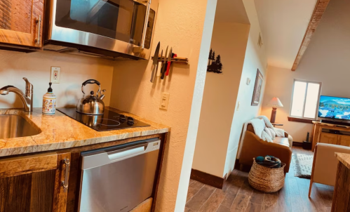 A cozy kitchen with a microwave, kettle, and sink, leading to a living area with a TV and comfortable seating.