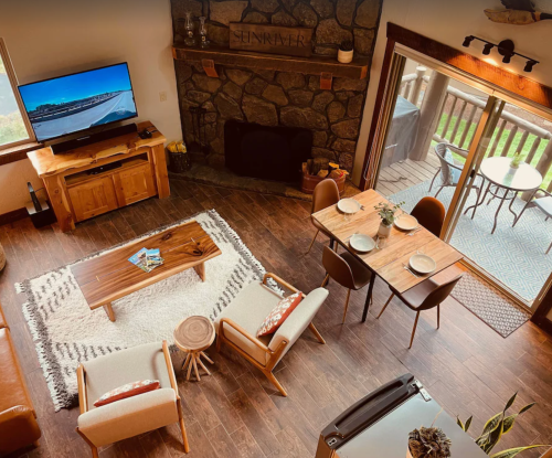 Cozy living room with a stone fireplace, TV, wooden furniture, and a dining area with a table and chairs.