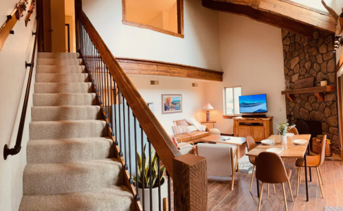 Cozy interior of a home featuring a staircase, living area, dining table, and stone fireplace. Warm, inviting atmosphere.
