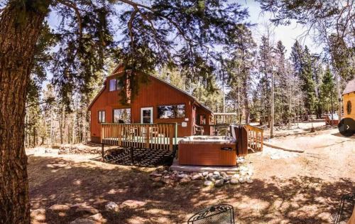 A cozy cabin surrounded by trees, featuring a deck and a hot tub in a serene outdoor setting.
