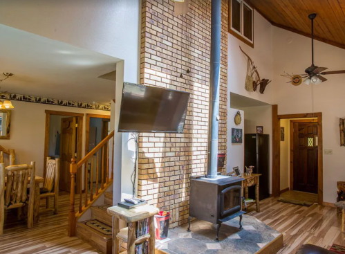 Cozy living space featuring a brick fireplace, wooden accents, and a TV, with a view of the dining area and entrance.