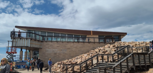 Pikes Peak Summit Visitor Center with rocky landscape and visitors, under a partly cloudy sky.