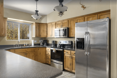 Modern kitchen with wooden cabinets, stainless steel appliances, and a countertop, featuring natural light from a window.