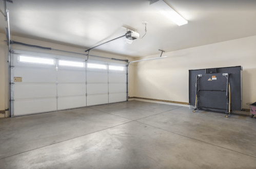 A spacious, empty garage with a large door, concrete floor, and a black storage unit in the corner.