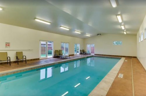 Indoor swimming pool with lounge chairs, large windows, and bright lighting.
