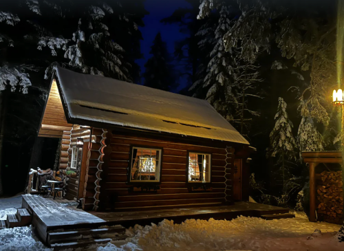 A cozy log cabin surrounded by snow-covered trees at night, with warm light glowing from the windows.