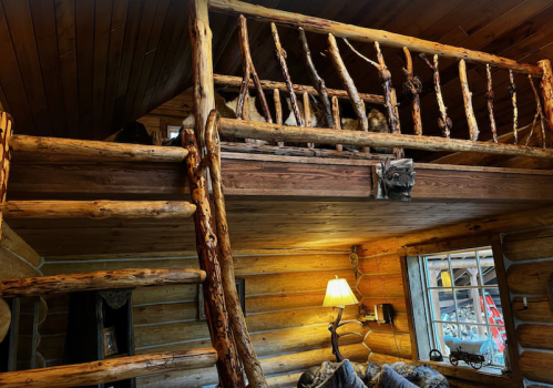 A cozy log cabin interior featuring a wooden loft, rustic railing, and warm lighting.