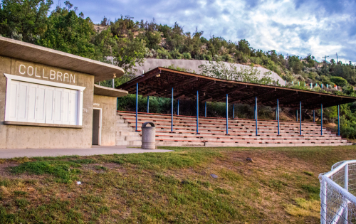 A concrete building with "COLLBRAN" signage next to a grassy area and a covered seating area on a hillside.