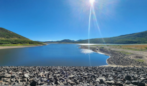 A serene lake surrounded by mountains under a clear blue sky, with sunlight reflecting on the water's surface.