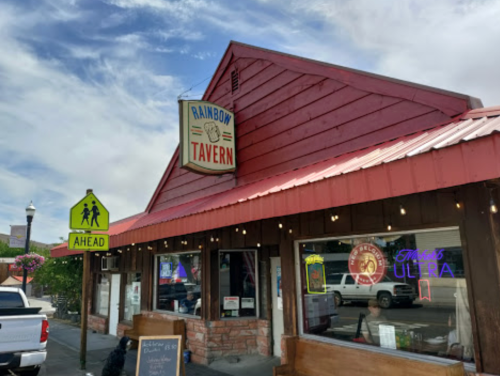 Exterior of Rainbow Tavern with a red roof, colorful signage, and a pedestrian crossing sign nearby.