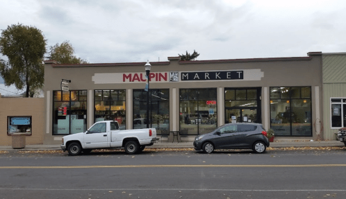 Exterior view of Malpin Market with two parked cars in front and a cloudy sky overhead.