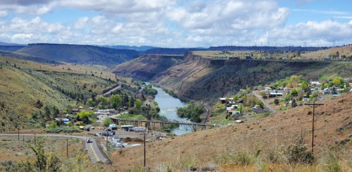 A scenic view of a river valley surrounded by hills, with a small town and bridge visible in the foreground.