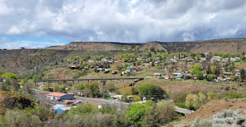 A scenic view of a small town nestled in a valley, surrounded by hills and greenery under a cloudy sky.