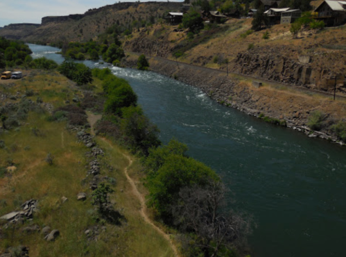 A winding river flows through a rocky landscape with greenery and distant houses on the hillside.