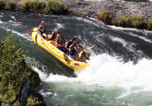 A group of people white-water rafting in a yellow raft, navigating through turbulent waters surrounded by greenery.