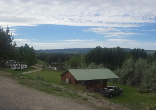 A scenic view of a rural landscape with a red cabin, green trees, and mountains in the distance under a cloudy sky.