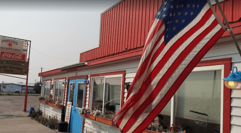 A quaint restaurant with a red roof, American flag, and flower boxes, featuring a sign for burgers and seafood.