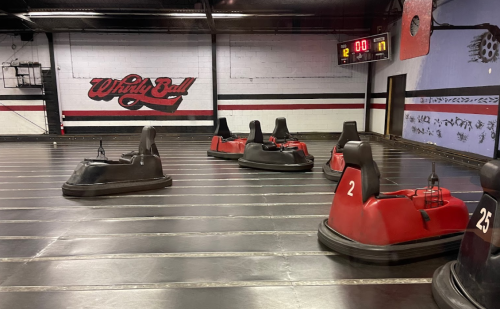 A WhirlyBall court with several bumper cars on a smooth floor, featuring a scoreboard in the background.
