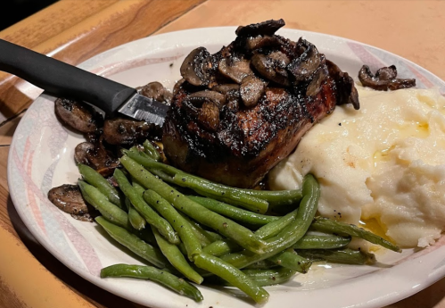 A plate of grilled steak topped with mushrooms, served with green beans and mashed potatoes.