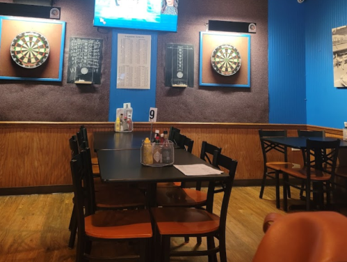 A cozy restaurant interior with a table set for dining, dartboards on the wall, and a TV in the background.