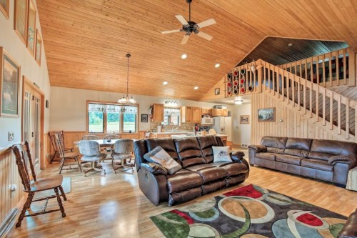 Cozy living room with wooden ceiling, leather sofas, dining area, and staircase, featuring a colorful area rug.