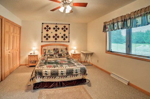 Cozy bedroom with a quilted bedspread, wooden furniture, and large windows overlooking greenery.