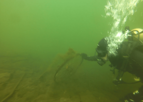 A diver exploring an underwater scene with murky green water and a submerged bicycle wheel.
