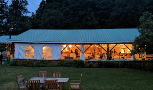 A cozy outdoor venue with string lights, set in a lush garden, hosting a gathering at dusk.