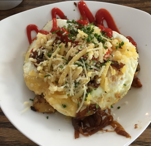 A plate of eggs topped with cheese, herbs, and ketchup, served over seasoned potatoes.