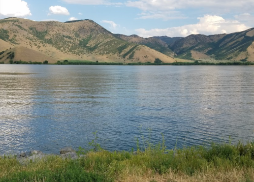 A serene lake surrounded by rolling hills and mountains under a partly cloudy sky.