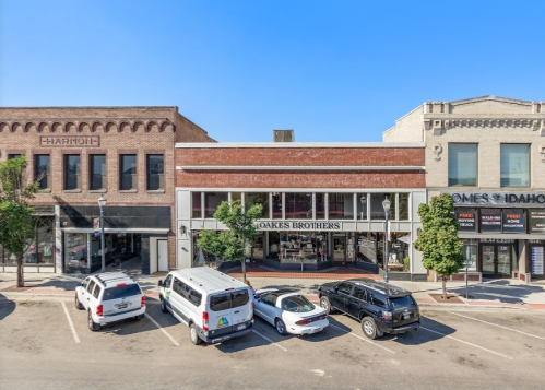 A view of a downtown street with parked cars and historic buildings, including Coakes Brothers and other shops.
